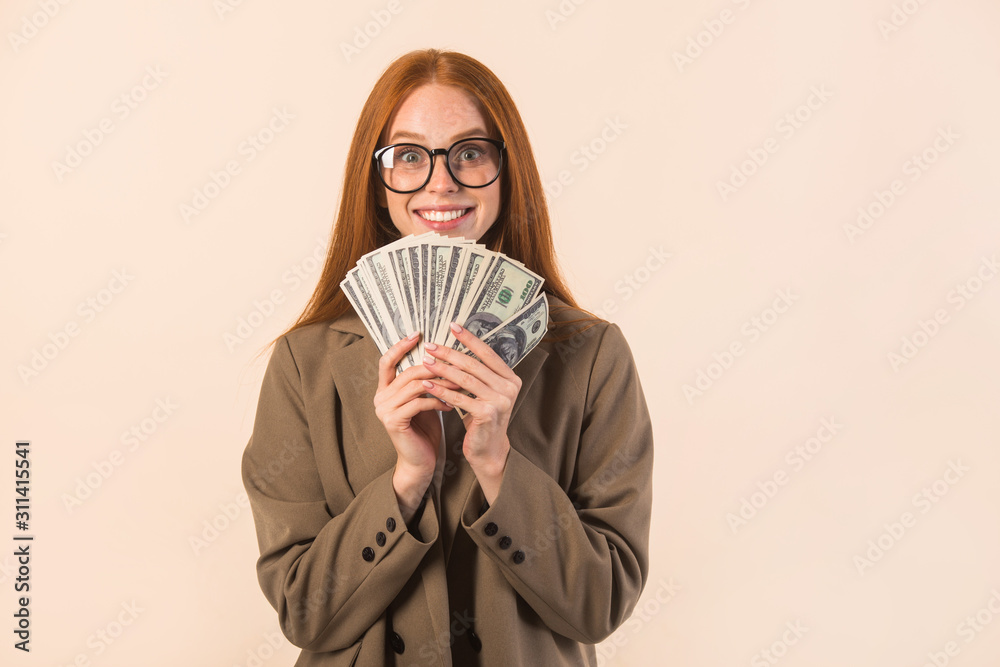 beautiful young woman with red hair in a jacket on a beige background with dollars in hands beautiful young woman with red hair in a jacket on a beige background with dollars in hands