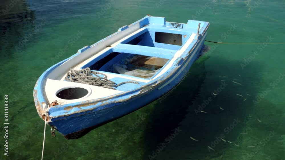 An old wooden boat of blue color is moored to the pier and floats on the surface of the clear sea water. Greece. 4K An old wooden boat of blue color is moored to the pier and floats on the surface of the clear sea water. Greece. 4K