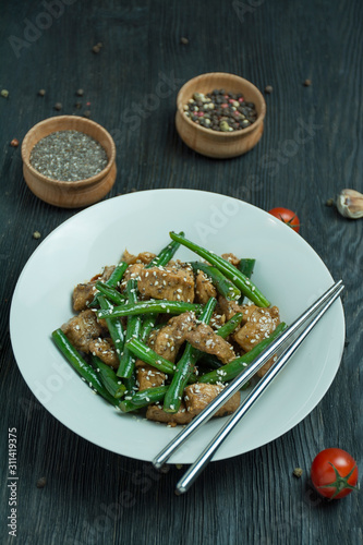 Salad of green beans and meat, sprinkled with sesame seeds. Serving of hot salad with green beans. Asian food. Dark wooden background. Space for text.