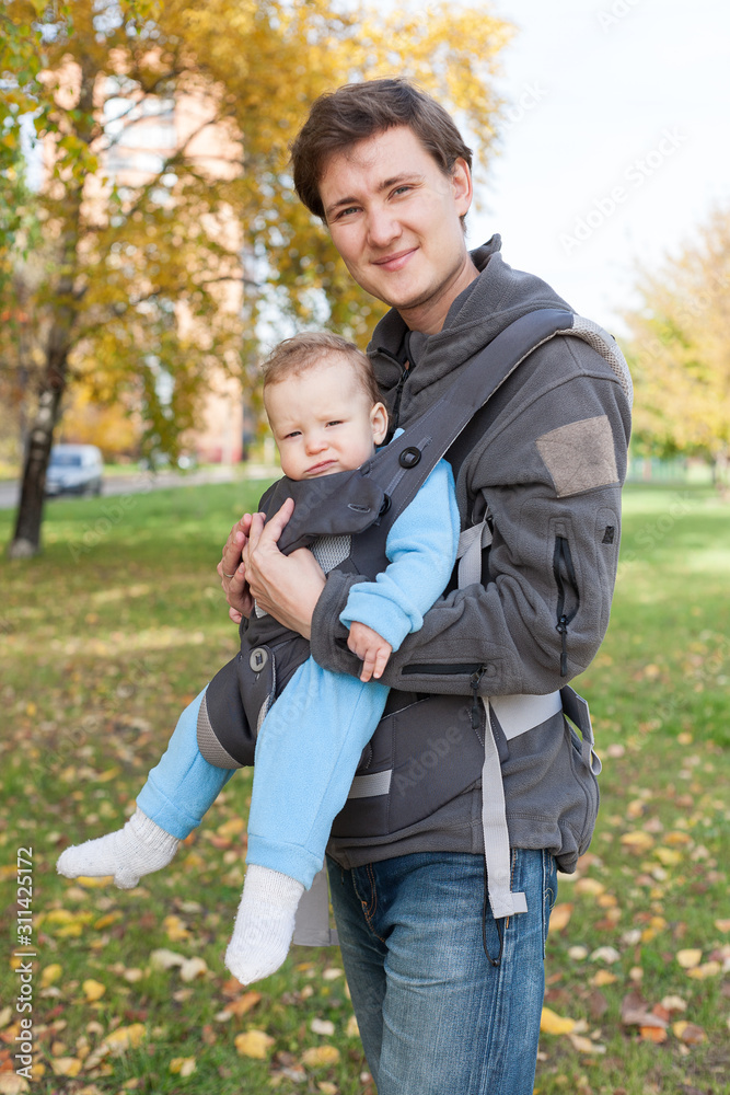 Fototapeta premium little toddler baby sits in the sling ergorace father, carrying child in an upright position without load on the spine