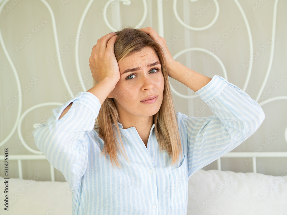 Fototapeta premium The emotion of suffering. Women with headache severely touch her head, sitting on the bed and looks into the camera. Female migraine