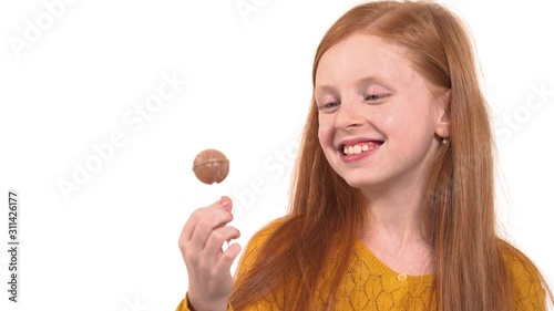 Close-up of foxy haired girl with green eyes eating candy. Little child eating sweet lollipop