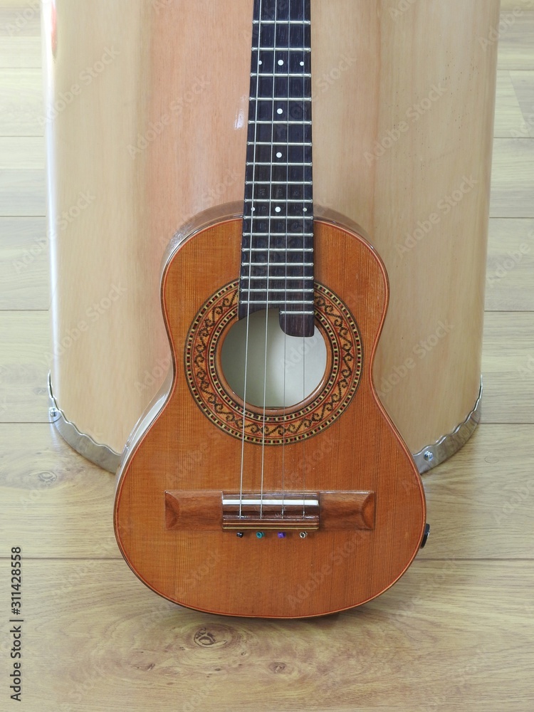 Obraz premium Close-up of a Brazilian stringed musical instrument, the cavaquinho, leaning against a drum, on a wooden surface. This instrument is widely used to accompany samba and choro, popular Brazilian rhythms