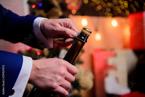 Open champagne and celebrate holiday. Celebrate new year with champagne drink. Toast and cheers concept. Male hands opening champagne bottle on christmas decorations background. Lets celebrate
