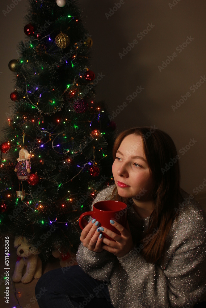 Beautiful young woman drinking tea at the Christmas tree. Beautiful girl celebrates Christmas with a cup of cocoa. Beautiful young woman drinking tea at the Christmas tree. Beautiful girl celebrates Christmas with a cup of cocoa.