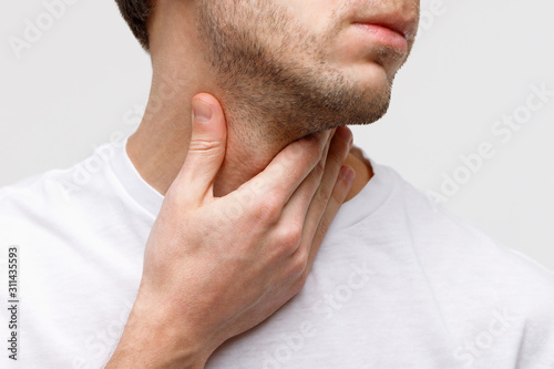 Close up of sick man suffering from throat problems, grey background, isolated. Thyroid gland, painful swallowing, pharyngitis, laryngeal swelling concept. Inflammation of the upper respiratory tract photo