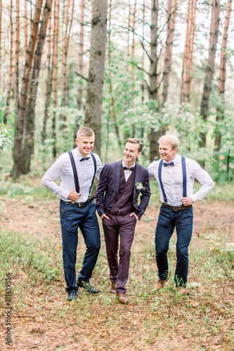 Cheerful stylish groom and groomsmen stand side by side, posing in the forest. Wedding shoot outdoors © sofiko14