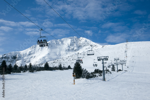 Panoramic wide angle view on white snowy ski slopes , mountain peak and ski chairlift transporting skiers. photo