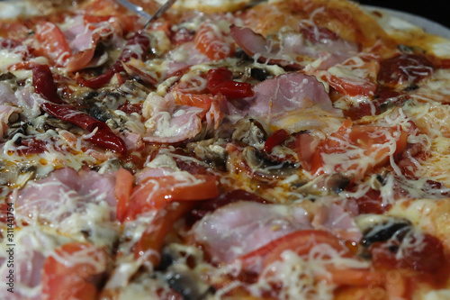 Big tasty and juicy pizza with cheese, bacon, tomatoes, pepper, spices on paper parchment close-up in a cafe. View from above. Italian pizza. Fast food concept. Free space for your text.