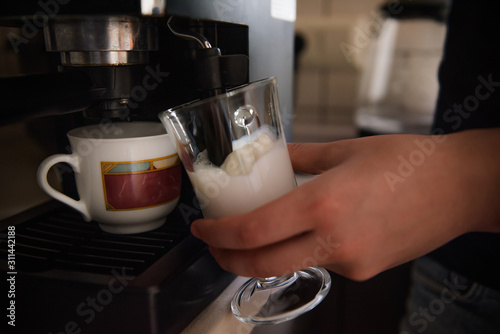 The hands of a young man make coffee from a coffee machine. Morning latte for breakfast at home. Homemade barista cappuccino in a stylish kitchen. Close up  place for text  copy space