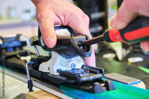 Obraz na płótnie Adjusting a ski binding rear piece release tension spring, using a flathead screwdriver - close up of ski service worker hand. w salonie