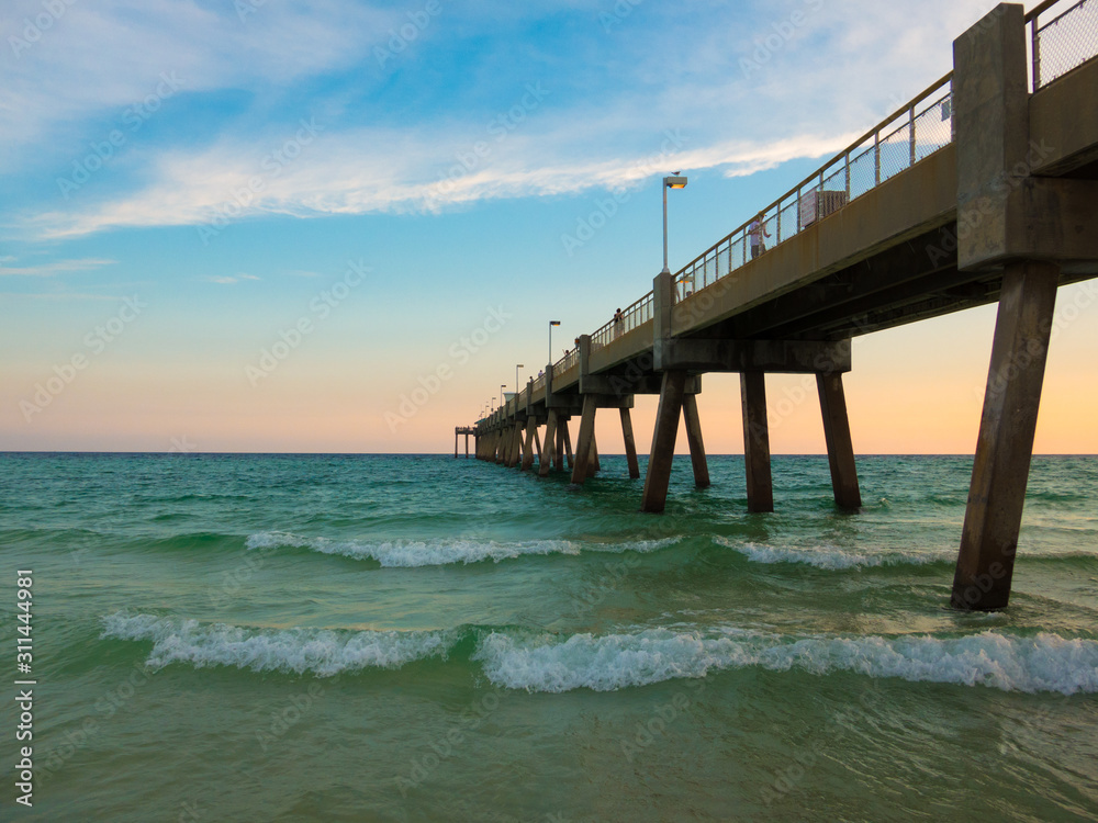 Pensacola beach with turquoise waters waves and pier entering into gulf of Mexico