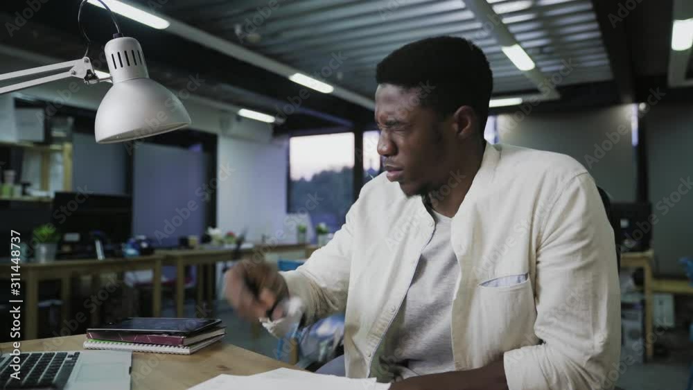 Young African man in glasses sitting at the office table and reading documents Young African man in glasses sitting at the office table and reading documents
