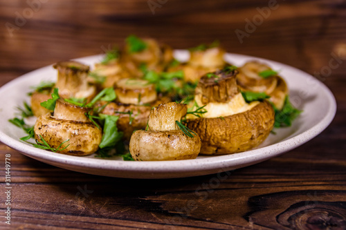 Plate with baked champignons, dill and parsley on a wooden table