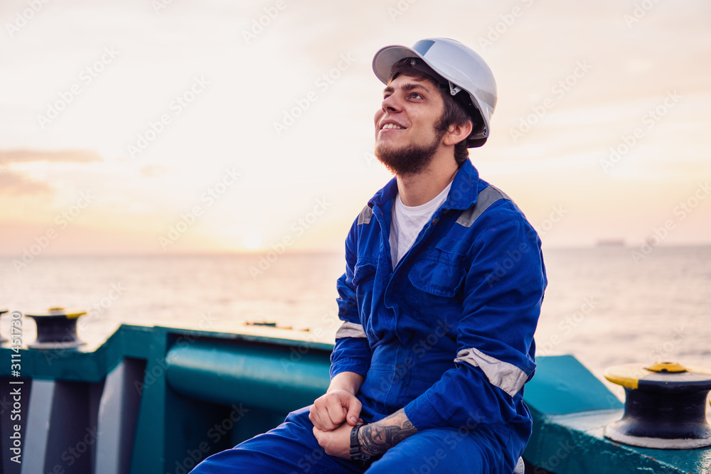 Marine Deck Officer or Chief mate on deck of offshore vessel or ship , wearing PPE personal protective equipment - helmet, coverall. Sunset light