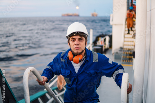 Marine Deck Officer or Chief mate seaman on deck of offshore vessel or ship , wearing PPE personal protective equipment - helmet, coverall. he climbs the ladder photo