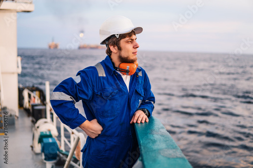 Marine Deck Officer or Chief mate on deck of offshore vessel or ship , wearing PPE personal protective equipment - helmet, coverall. Sea view