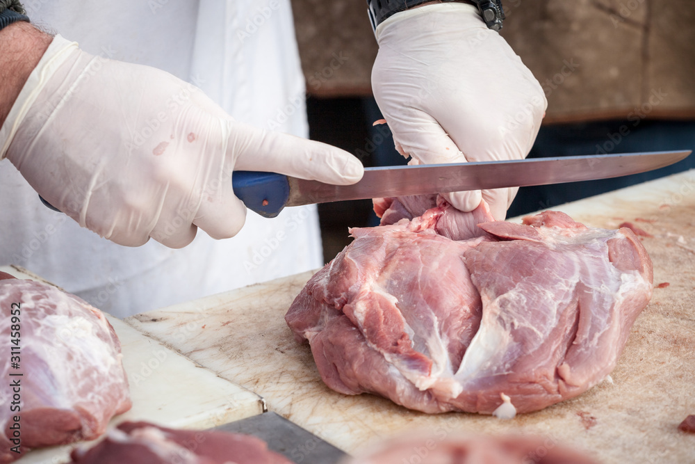 Hands Of A Professional Butcher Cutting A Piece Of Raw Pork Meat With A Long Knife