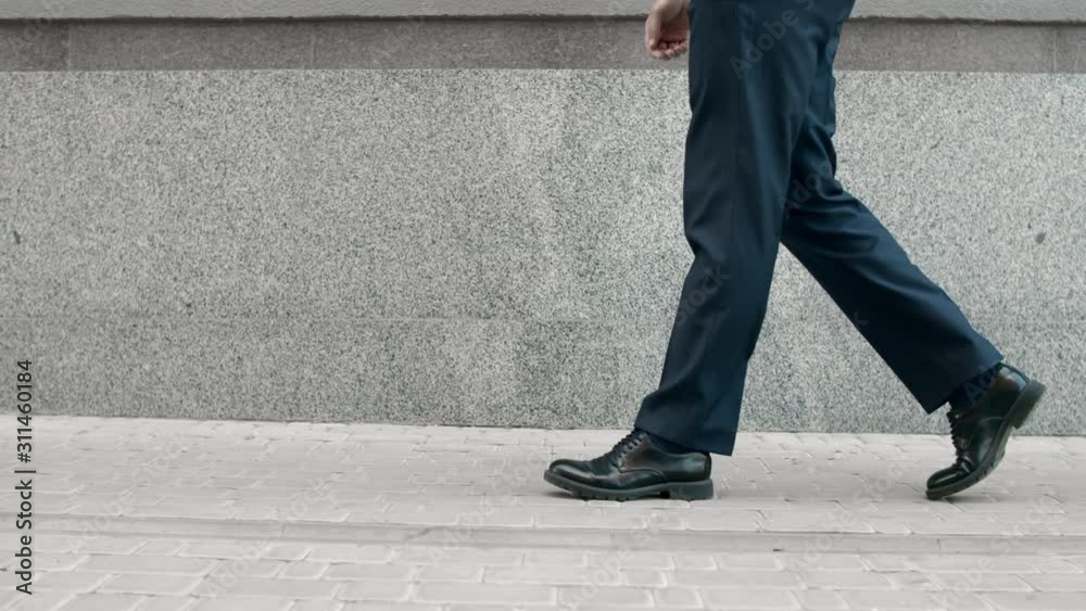 Cropped image man walking in black shoes. Closeup male feet going near building Cropped image man walking in black shoes. Closeup male feet going near building