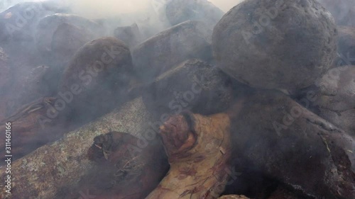 Mumu, traditional method of cooking large quantities of food for celebrations in Papua New Guinea, pork, chicken, lamb and roasted vegetables in a ground oven. Close up to the wood fire. photo