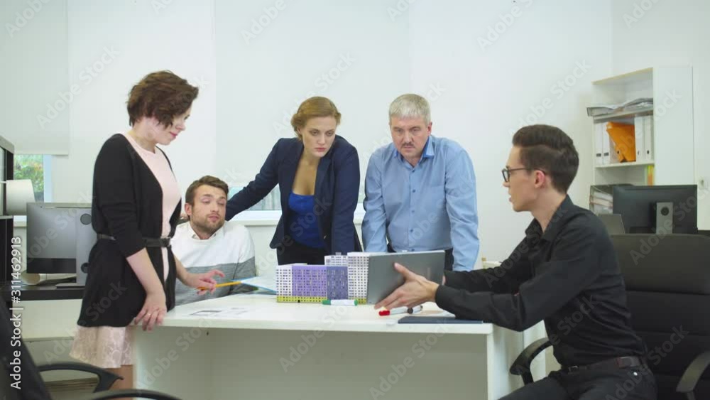 Engineer in glasses show something on tablet to his workmates Engineer in glasses show something on tablet to his workmates