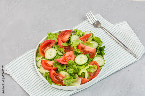 Healthy vegetarian dish on table, vegetable salad with fresh tomato, cucumber, lettuce, red onion on gray concrete background. Diet menu. Top view. Flat lay, mockup, template with copy space