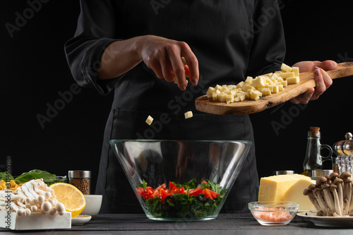 Chef sprinkles squares of mazarella cheese in a bowl with salad,. Freeze in motion, Salad, organic ingredients and products. Vegetarian and tasty food. Advertising photo of food