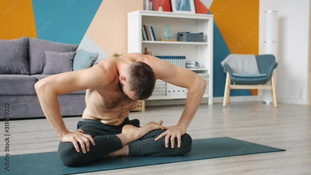 Topless guy is execising abdomen muscles practising yogic breathing technique at home sitting on yoga mat moving belly. People and healthy lifestyle concept. Topless guy is execising abdomen muscles practising yogic breathing technique at home sitting on yoga mat moving belly. People and healthy lifestyle concept.