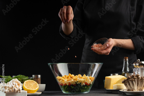 Fototapeta Naklejka Na Ścianę i Meble -  A professional chef cooks a fresh and healthy salad by sowing coarse salt, Freezing in motion. Organic and wholesome food. Healthy nutrition and vitamins. Advertising photo, on black background.