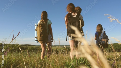 Happy mom and daughters, a little baby travel across the field with backpacks in colors in the summer. Family life. Tourist girls and a little baby go camping in the forest. Teamwork travelers. © zoteva87