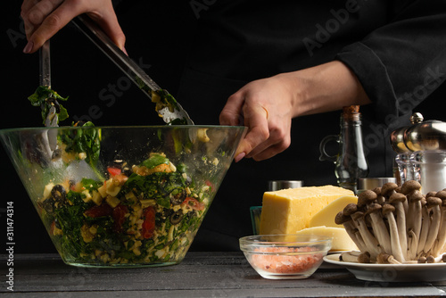 A professional cook prepares a fresh salad with spinach leaves, mixes the salad on the background with fresh ingredients, Freezing in motion. Vegetarian and healthy food. Organic food