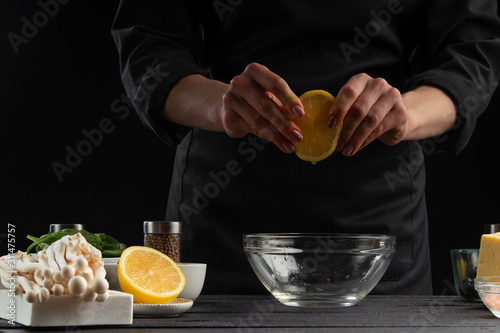 Cooking sauce or salad dressing. With ingredients. On a black background. The chef cooks a lemon, getting juice.