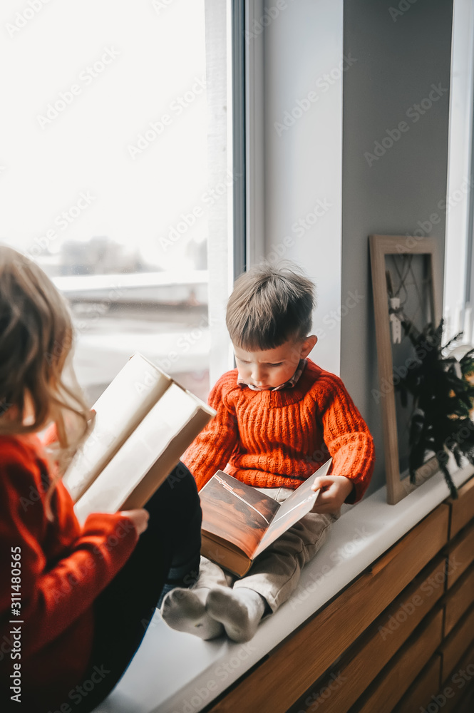 Cute children reading books on sill near window