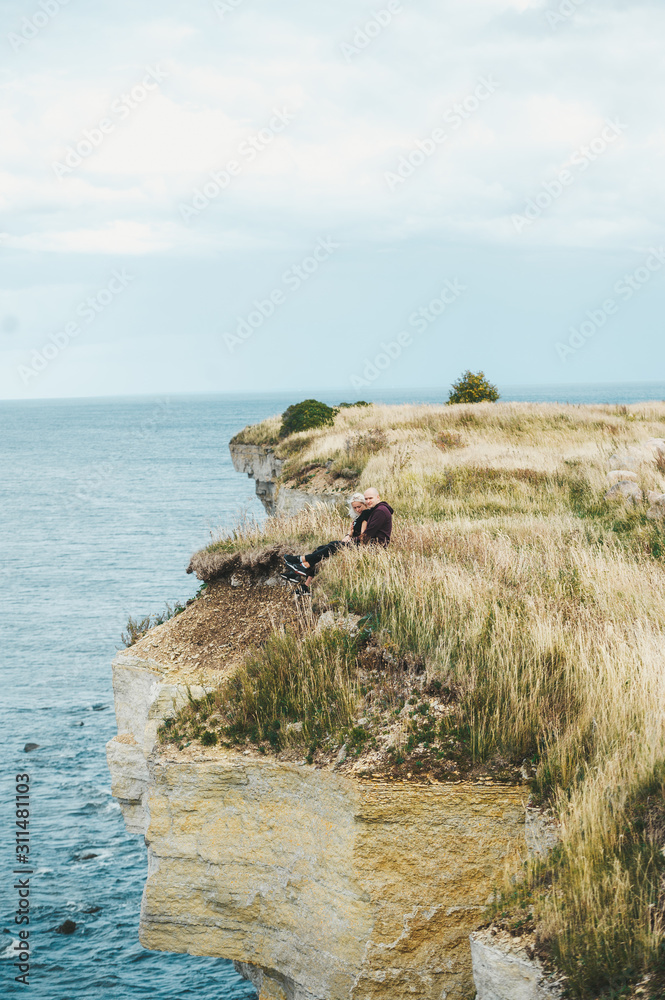 A couple sitting on grass on the edge of the rocky coast of the Baltic sea.