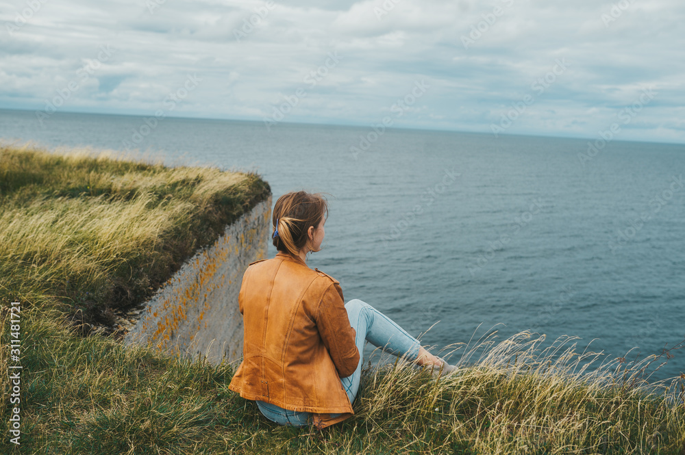 A woman standing on grass on the edge of the rocky coast of the Baltic sea. Rear view