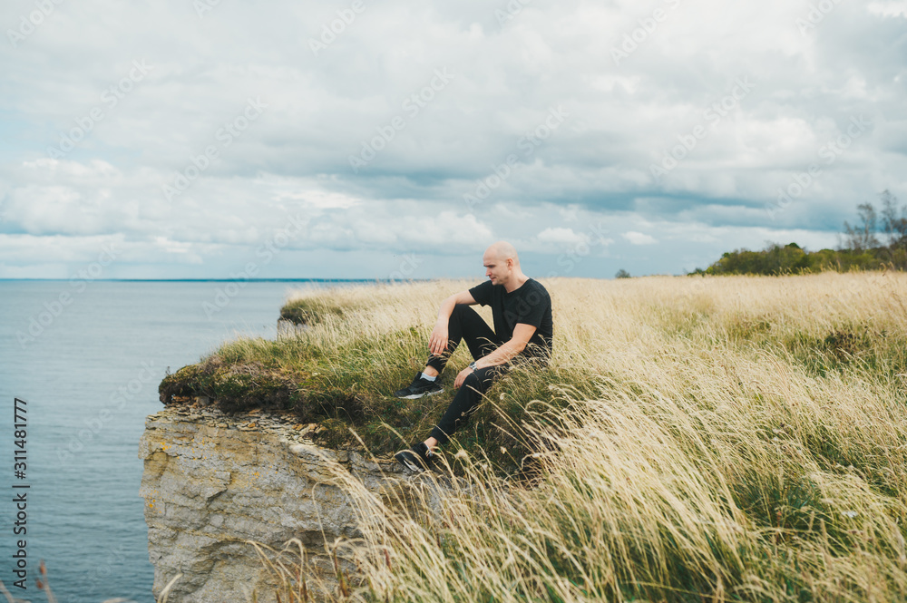 A tourist spending time on grass on the edge of the rocky coast of the Baltic sea A tourist spending time on grass on the edge of the rocky coast of the Baltic sea