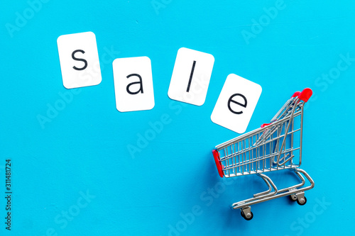 Sales message. Text Sale near shopping trolley chart on blue background top-down copy space