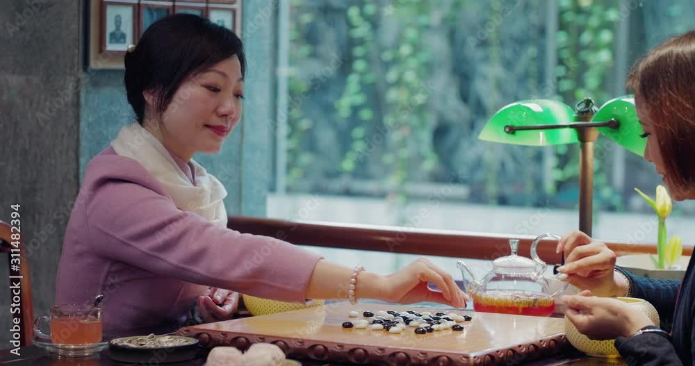 two smart Chinese ladies playing the game of go together at home, happy friends playing chess thinking strategy in the library, chess enthusiast playing Chinese chess together
