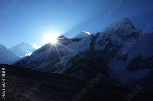 Everest trek, On the way to Kala Patthar - first sun shining from behind mountains, (Everest is in the middle with shiny blowing away snow). Sagarmatha national park, Solukhumbu, Nepal