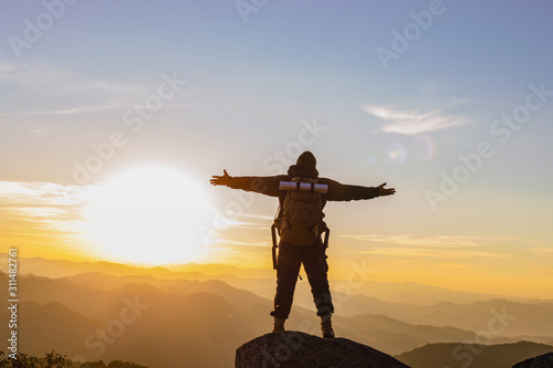 Successful people concept.Young man with backpack raised hands on top of mountain layers line enjoying valley view.