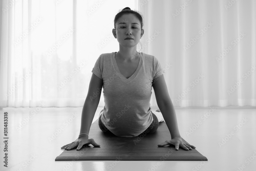 Asian yogi woman practicing yoga concept, stretching in Cobra exercise, Bhujangasana pose, working out, indoor full length, white yoga studio ,concept of healthy life and natural balance,Front view