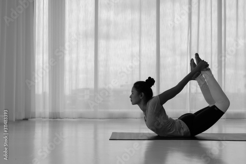Side view Asian woman working out in fitness club or at home, doing yoga or pilates exercise. Dhanurasana, Bow pose,Full length, Concept of healing body and spirit,copy space,monochrome