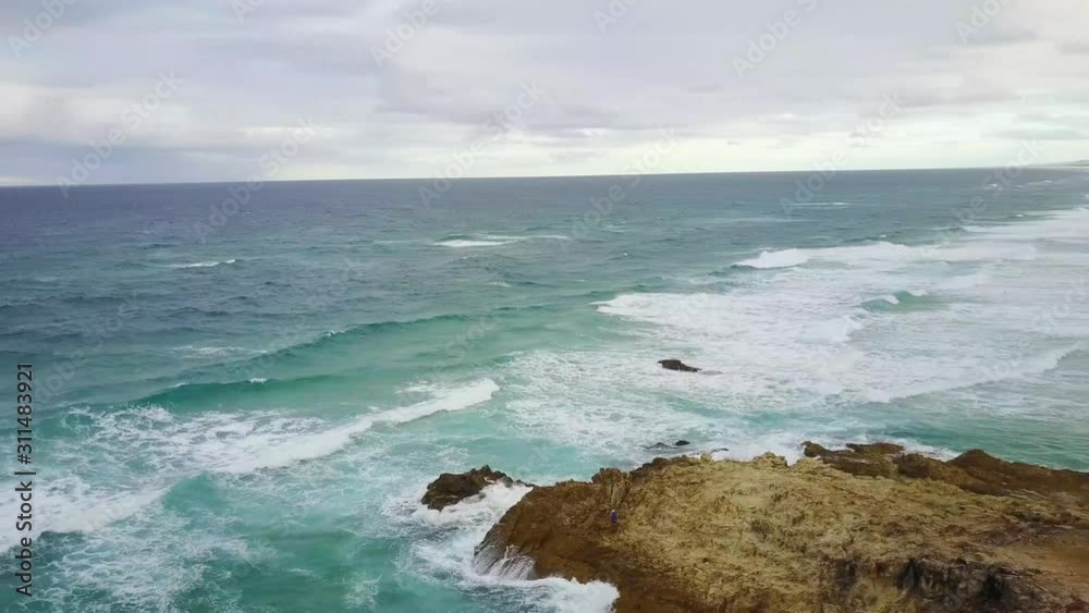 Aerial Drone Above A Beach On An Overcast Day With Blue Waves Crashing Onto The Shore Aerial Drone Above A Beach On An Overcast Day With Blue Waves Crashing Onto The Shore