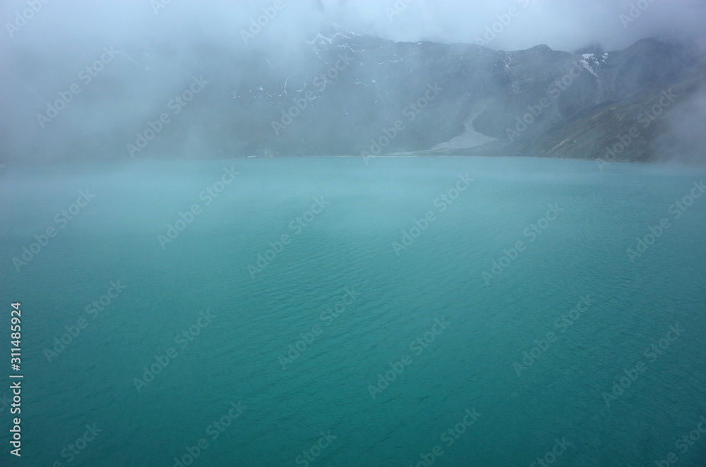 Fototapeta premium Hiking in Nepal Himalayas, Gokyo lake (4870 m) in clouds in beginning of summer. High altitude glacier lake in mountains in cloudy weather