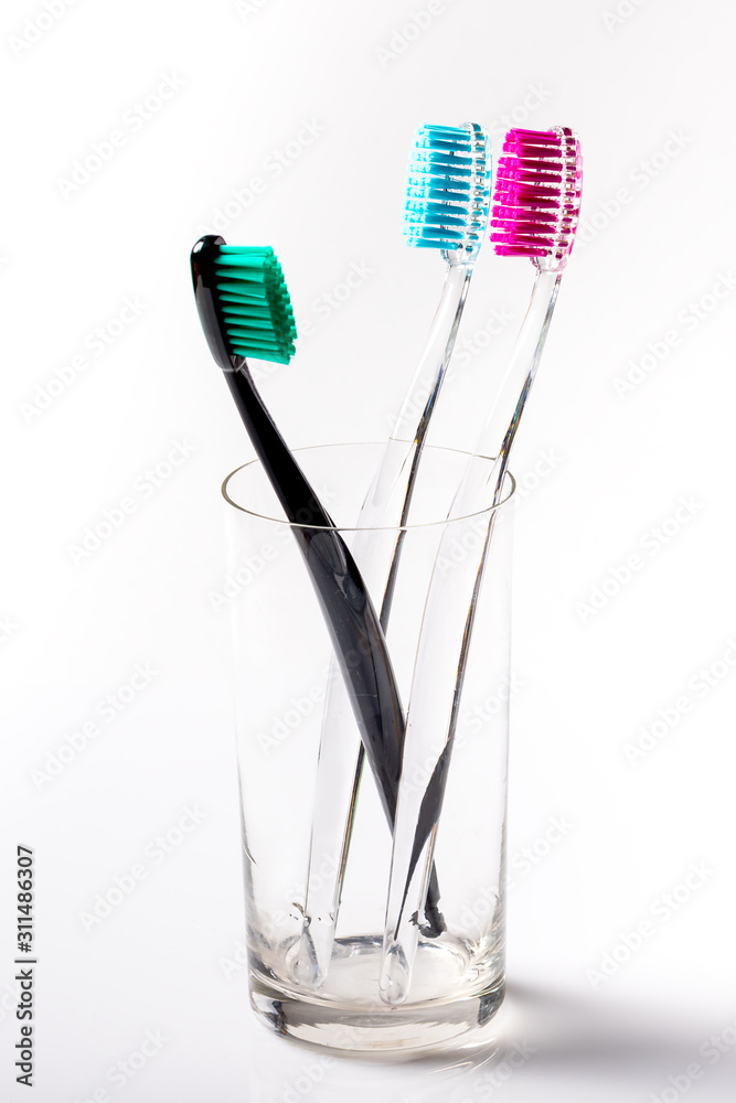 Toothbrushes of different colors in a glass beaker on a white background. Toothbrushes of different colors in a glass beaker on a white background.