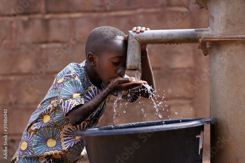 Young African Boy Drinking Water From The Community Borehole Hand Pump photo