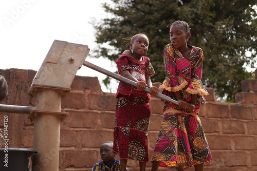 Принти на полотні Young Girls Helping Each Other Pumping Water At An African Village Borehole