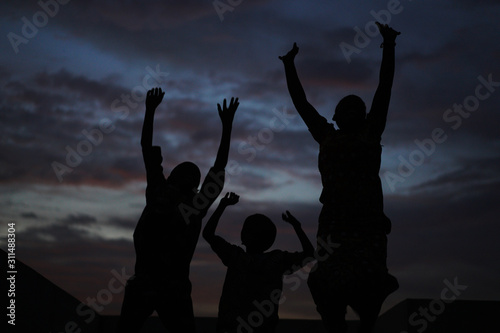 Night Scene With Silhouettes Of Joyful African Children Jumping In Their Courtyard With Hands Up 