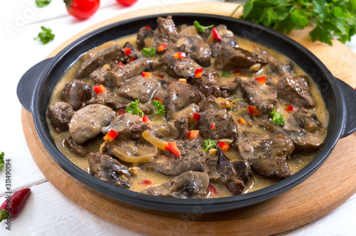 Turkey liver with onions and mushrooms in a creamy sauce on a white wooden background. Diet menu