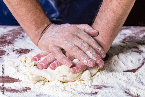 Сlose up of chef human's hands kneading the dough on the table, powdering with flour. Making dough by hands at bakery or at home.